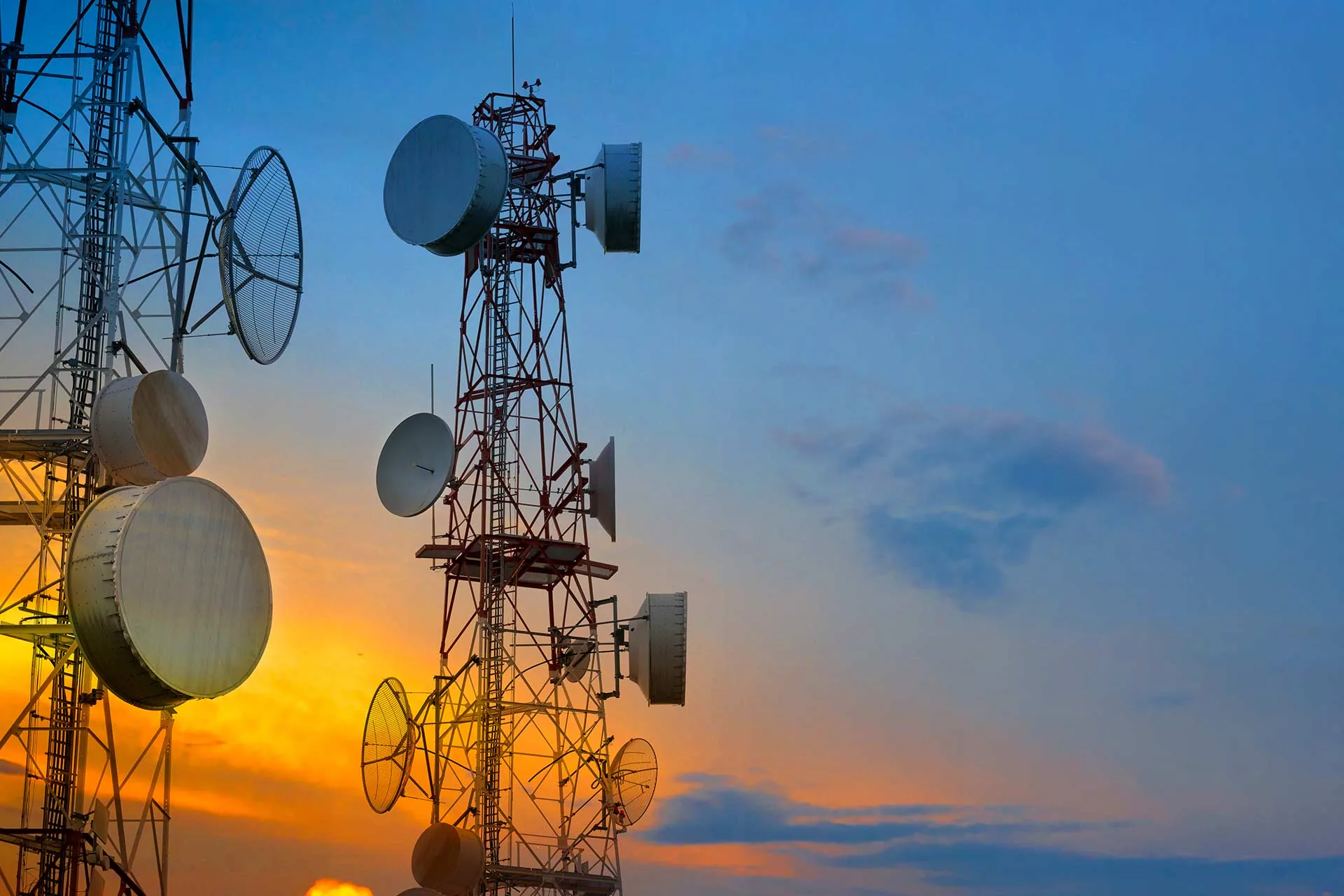 Telecom towers carrying antennas and microwave dishes at sunset